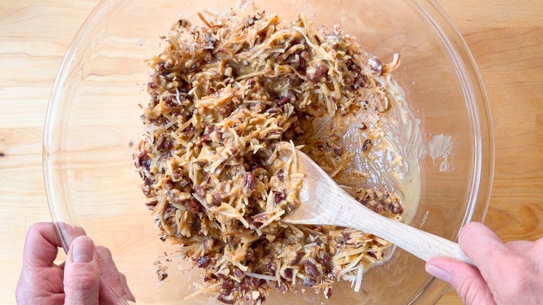 Mixing cooked custard into toasted shredded coconut and chopped pecans in glass bowl