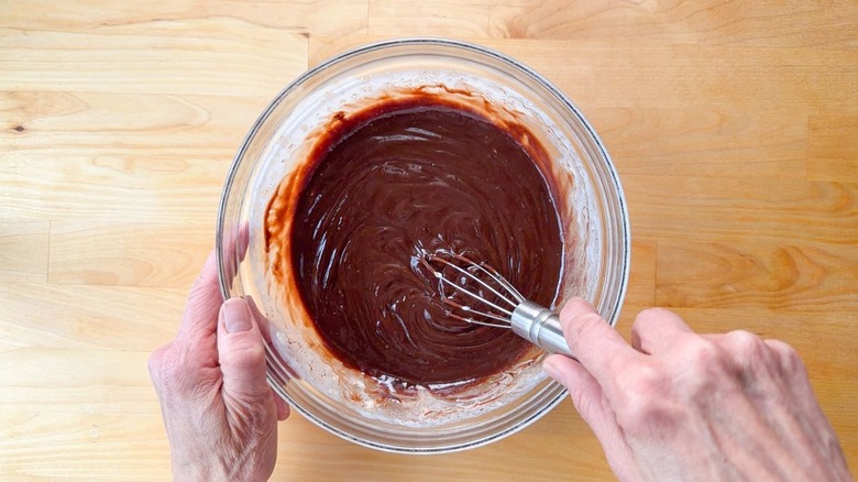 Whisking chocolate ganache in glass bowl on countertop