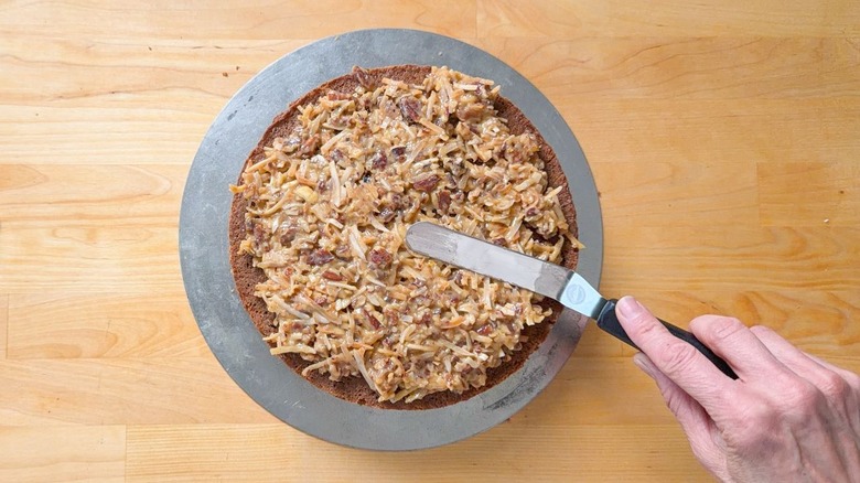 Spreading German chocolate cake filling on a German chocolate cake layer with an offset spatula
