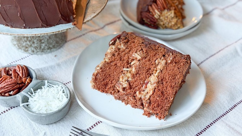 German chocolate cake slice on plate with coconut and pecans on the side