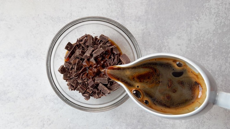 Pouring hot espresso over chopped chocolate in glass bowl