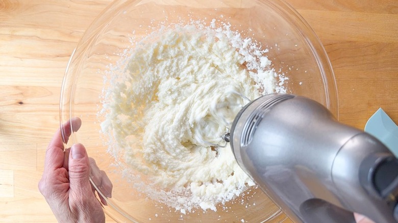 Creaming together sugar, butter, and oil with a hand mixer in a glass bowl