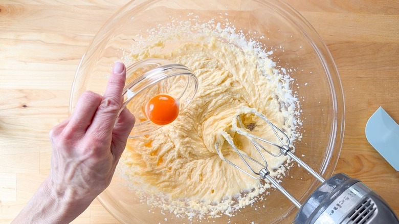 Adding an egg yolk to creamed sugar and butter in a glass bowl