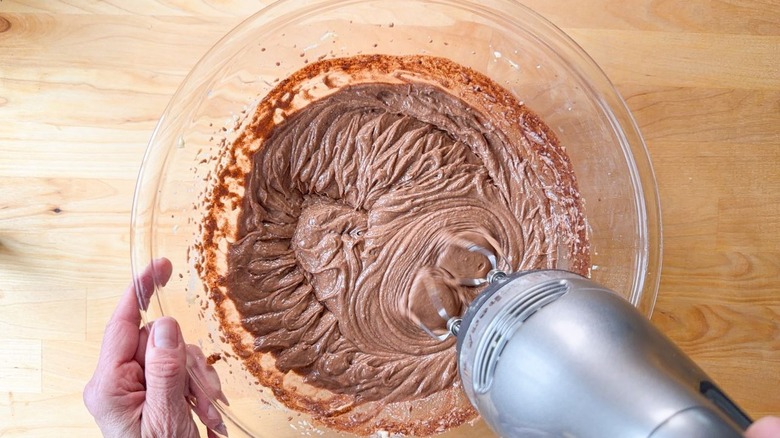 Mixing chocolate, butter, and sugar with a hand mixer in a glass bowl
