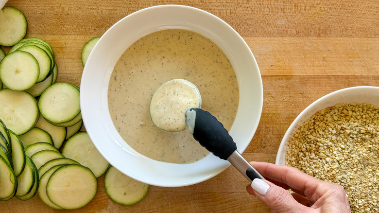 hand dipping zucchini in dressing