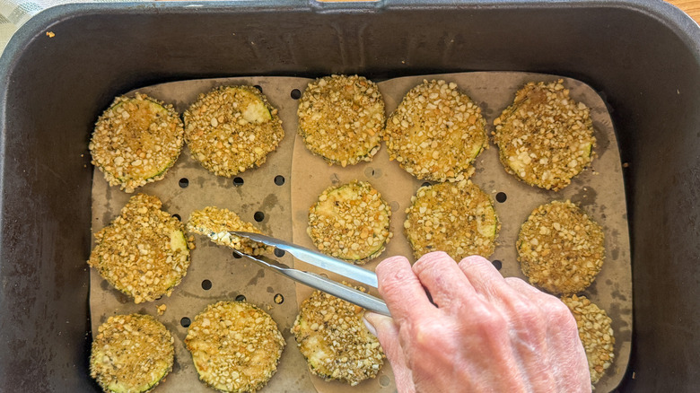 hand flipping over zucchini in air fryer basket