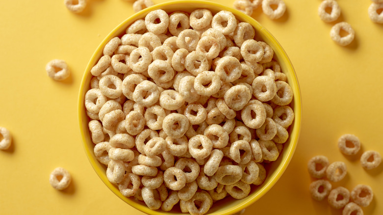 cheerios cereal in a yellow bowl on a yellow background with cheerios scattered around