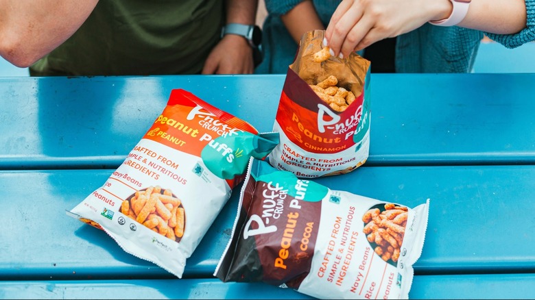 People eating from three bags of P-Nuff Crunch, overhead view on blue picnic table