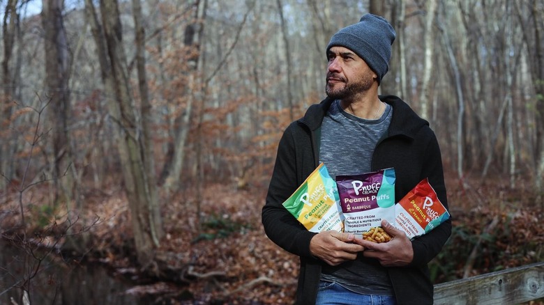 Juan Salinas holding three bags of P-Nuff Crunch in wooded area