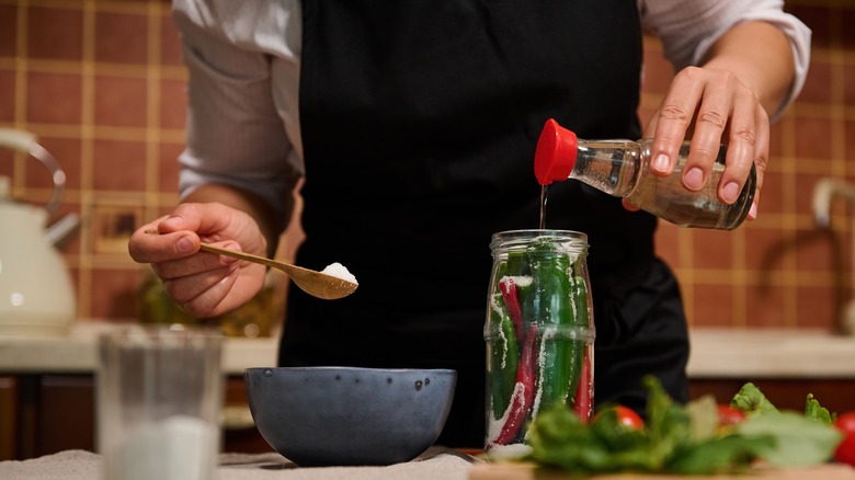 chef adding soy sauce and salt to a jar of peppers