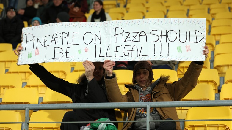 two people hold a sign denouncing pineapple pizza