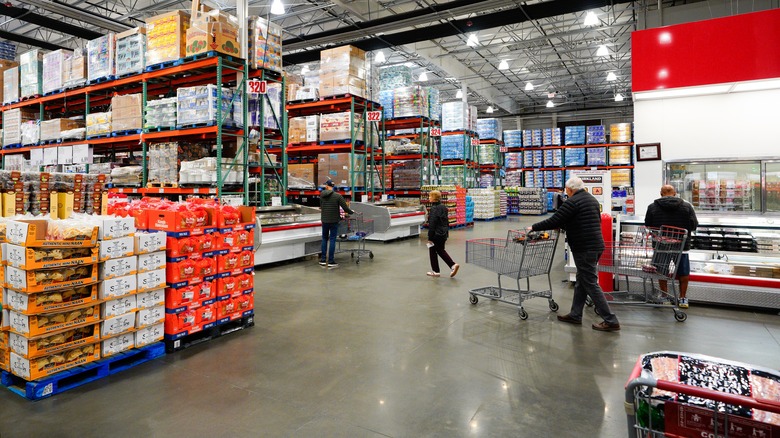 Shoppers inside a Costco store with large shelves and product pallets.