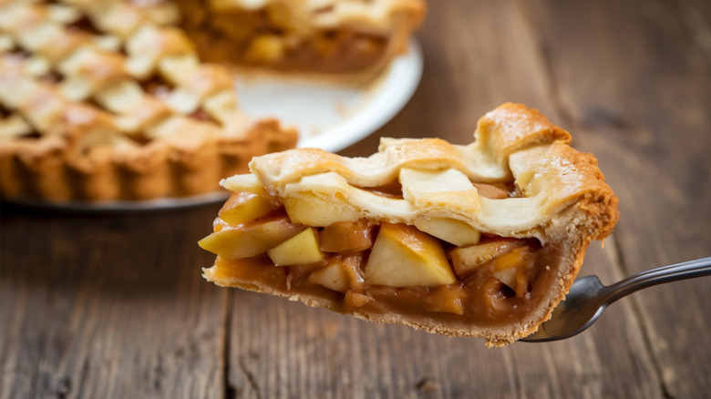 A close-up of a slice of apple pie held up on a fork