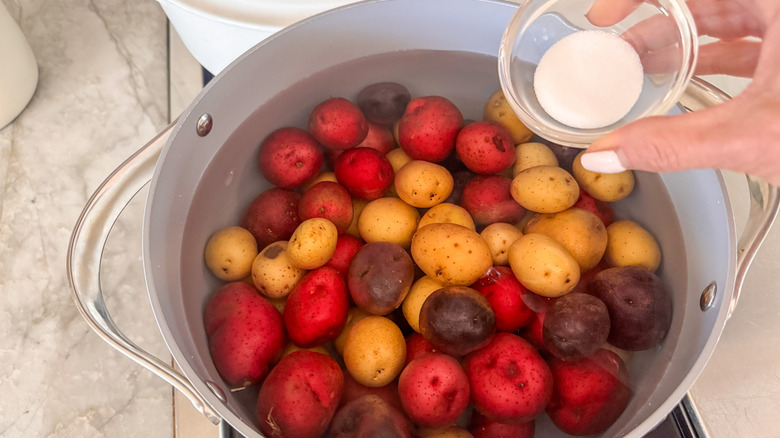 hand adding salt to potatoes