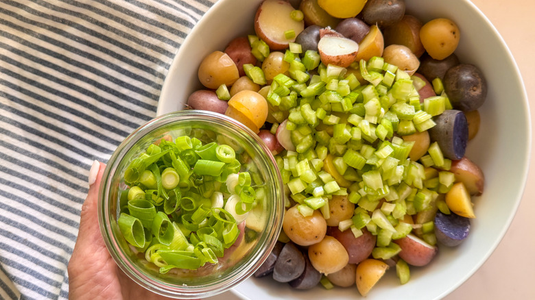 hand adding green onion to bowl