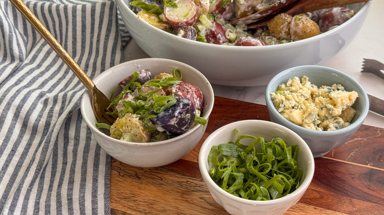 bowl of potato salad, green onions, and blue cheese on wooden board