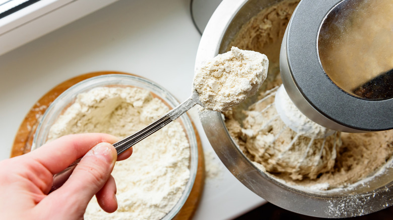 Hands using stand mixer to mix dough, adding flour.