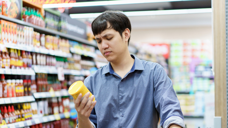 Man looks at label of product in grocery aisle.