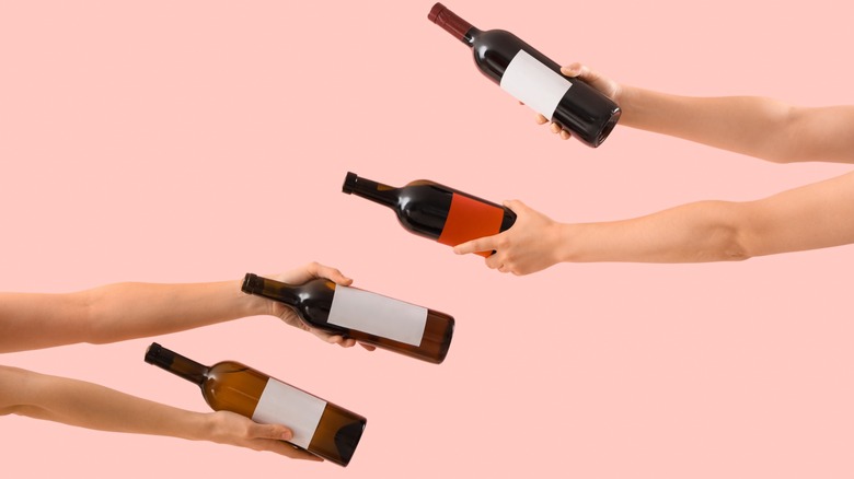 hands holding wine bottles against pink background