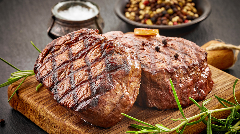 Grilled beef steaks with spices on a wooden cutting board.