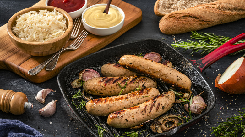Cooked brats in cast iron griddle and toppings on nearby cutting board