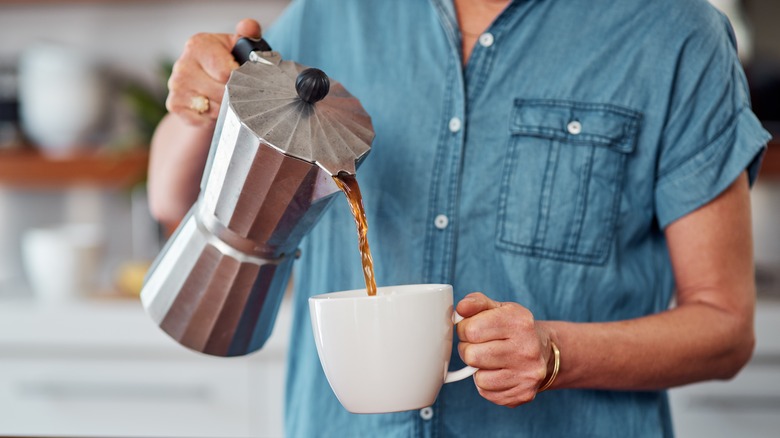 Closeup person pouring coffee into mug from percolator.