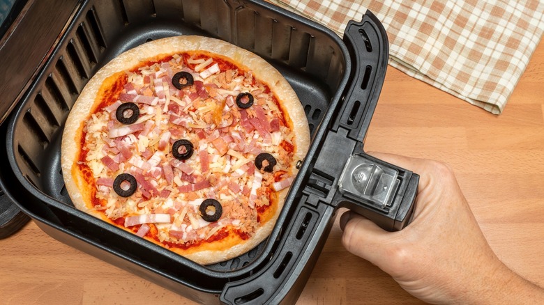 Person pulling air fryer basket out with pizza in it