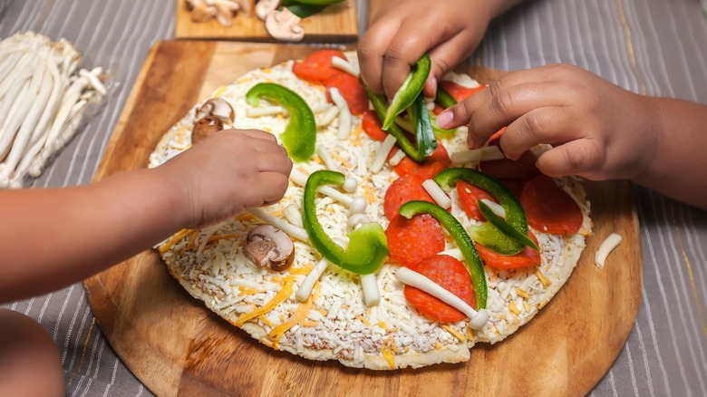 Children adding toppings to frozen pizza