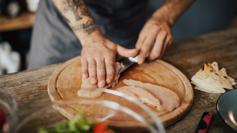 Person cutting raw chicken on cutting board