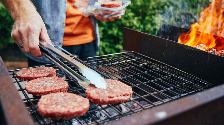 Someone laying raw burgers on a grill