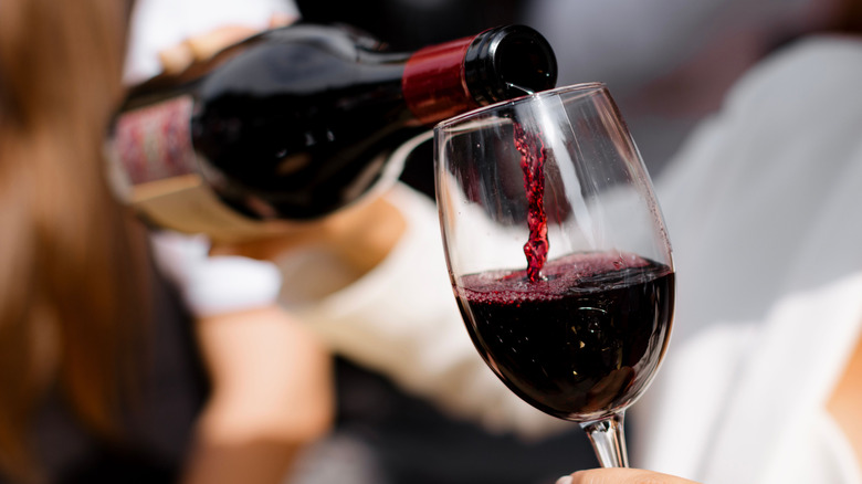 Someone pouring a glass of red wine into a glass
