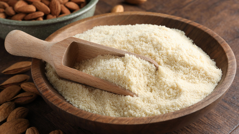 A wooden scoop in bowl of almond flour with nuts on a wooden table