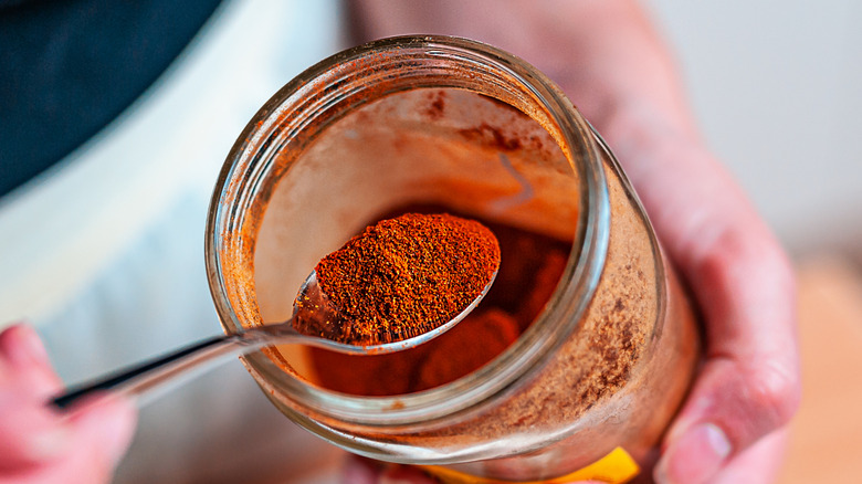 Someone spooning cayenne pepper out of a jar