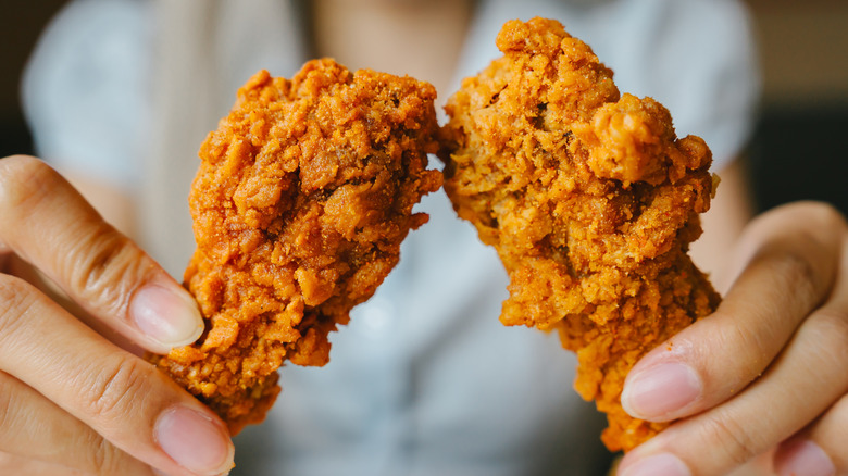 Closeup of hands holding two fried chicken drumsticks