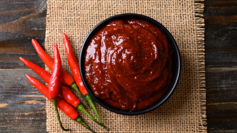 A small bowl of gochujang next to some chilis on a table