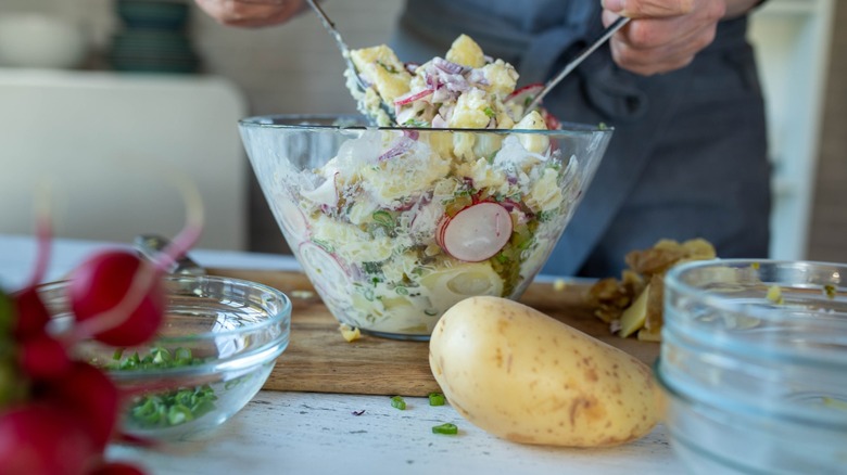 hands mix potato salad in a glass bowl