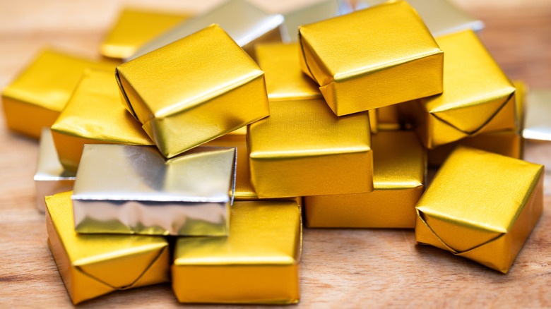 Gold and silver-wrapped bouillon cubes on wooden background