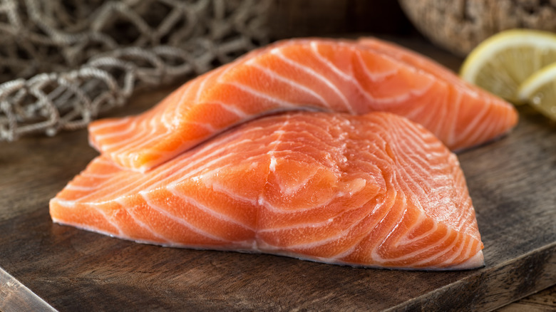Fresh salmon fillets on a wooden board with lemon and fish net background