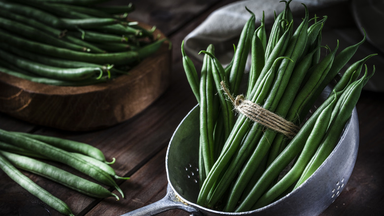 Green beans in a metal colander on a wooden table
