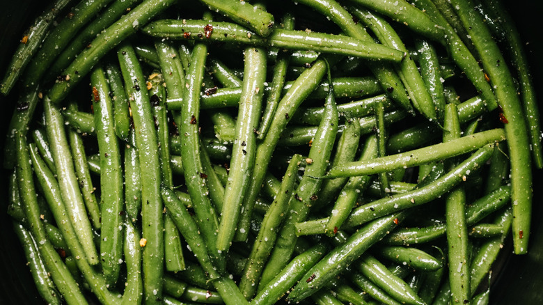 Seasoned raw green beans in an air fryer basket