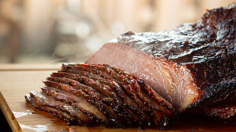 A close up of thinly sliced cooked brisket on cutting board.