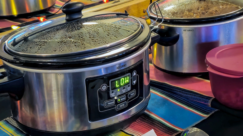 A slow cooker set to low on a striped tablecloth