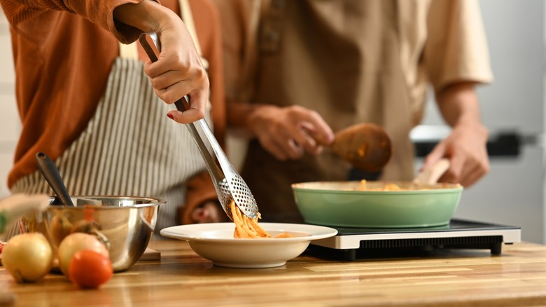 two adults cook pasta in a kitchen