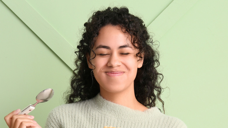 Smiling woman with spoon against green wall.