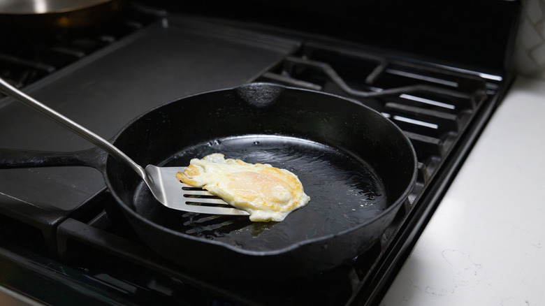 A metal spatula lifting a fried egg out of a cast iron skillet.
