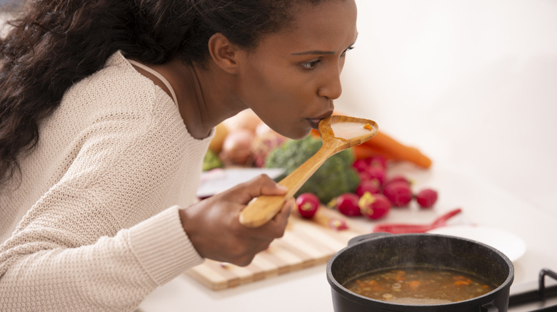 Woman tasting soup from pot.