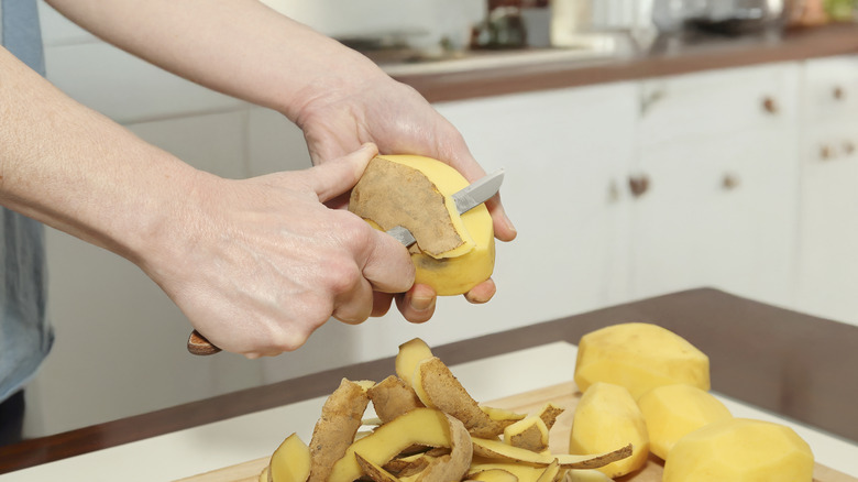 peeling yellow potatoes over cutting board