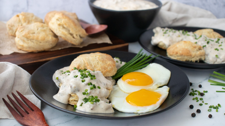 Side shot of a plate of biscuits and gravy with some fried eggs on the side
