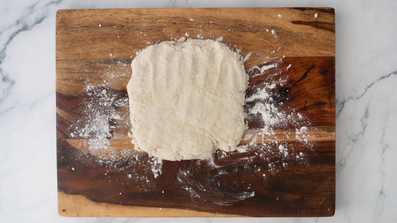 A rough square of dough on a wood cutting board