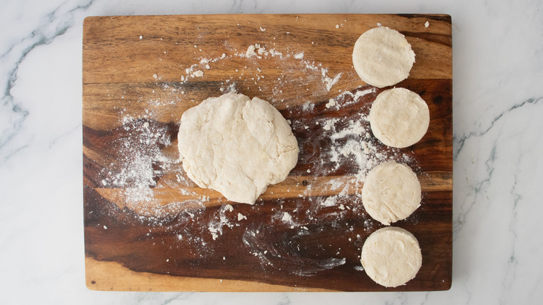 Reshaped biscuit dough next to portioned biscuits on a wood cutting board
